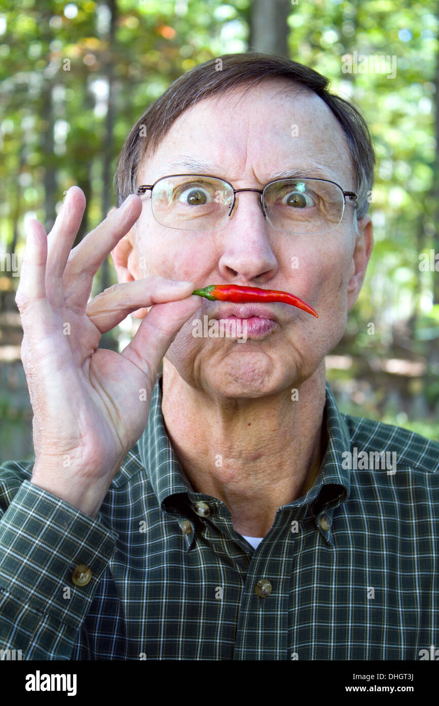Senior adult holds a red chili pepper under his nose in a mustache position with a silly look on his face. Stock Photo