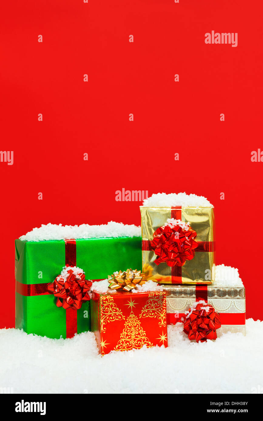 Snow covered Christmas gift wrapped presents against a red background. Stock Photo