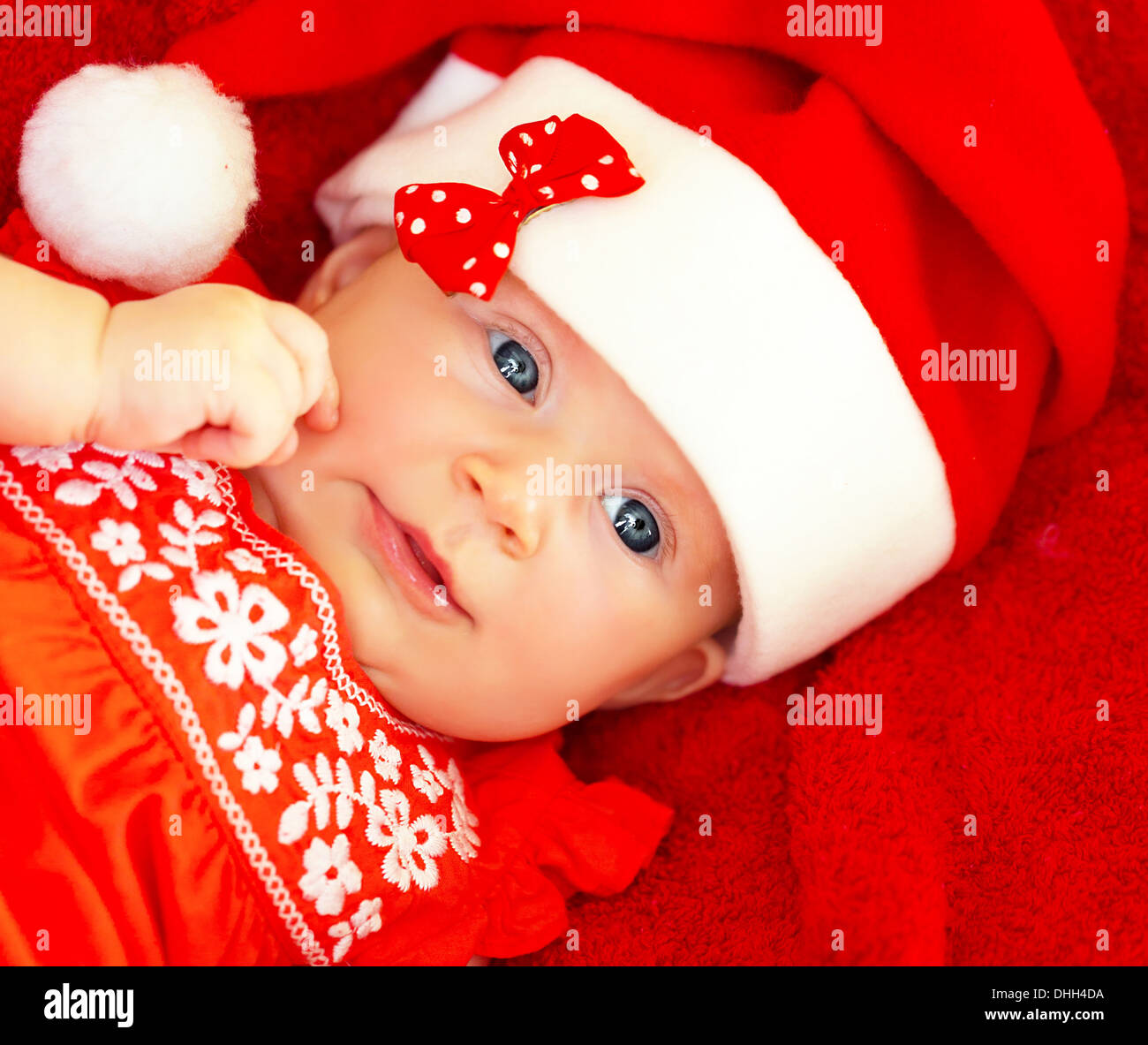 Closeup on beautiful newborn baby wearing red festive Christmas costume, Santa hat with decorative bow, New Year celebration Stock Photo