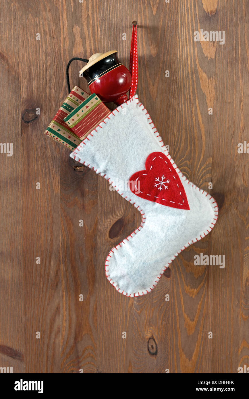 White Christmas stocking filled with traditional gifts and toys hanging by a rusty nail in an old door. Stock Photo