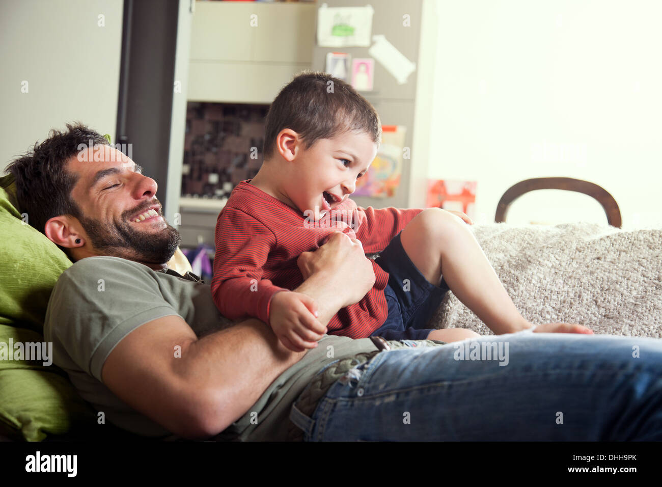 Father reclined on sofa with son on lap Stock Photo