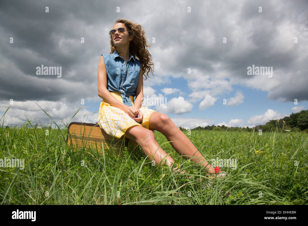 Teenage girl sitting on suitcase in field Stock Photo