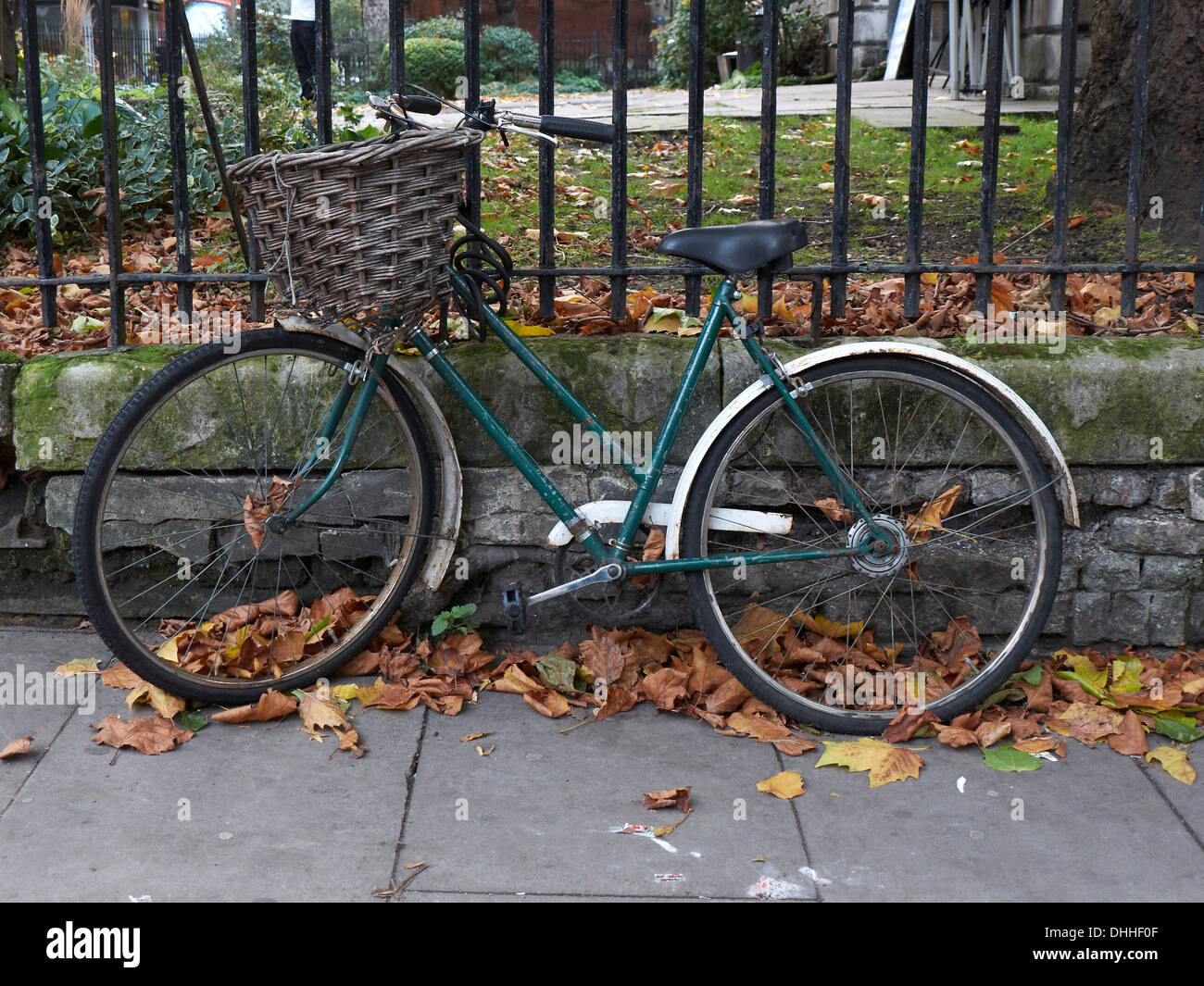 An old Bicycle with a wicker basket chained to railings leaning against the Railings of St Giles church in London Stock Photo