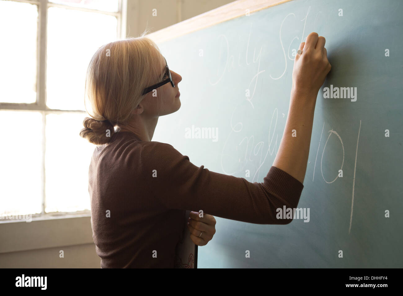 Teacher writing on blackboard with chalk Stock Photo