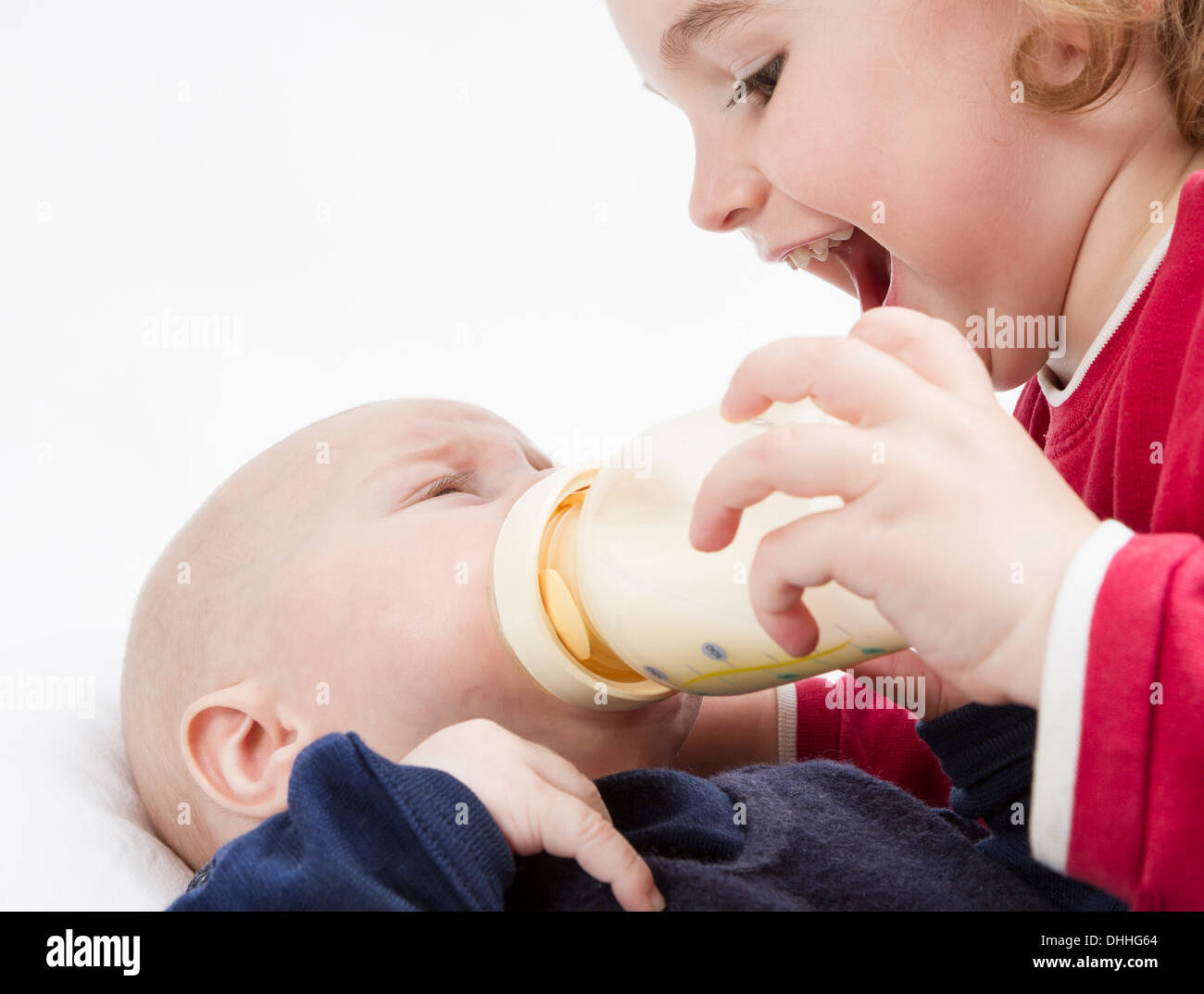 young, happy child feeding toddler with milk bottle in light background Stock Photo