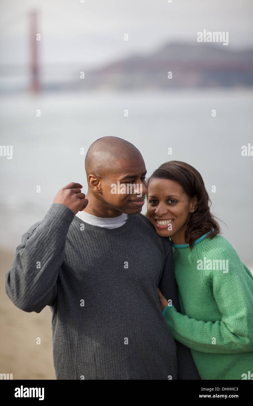 Mixed bald and haired couple frolic on the sandy beach under the stern gaze of an out of focus Golden Gate Bridge. Stock Photo