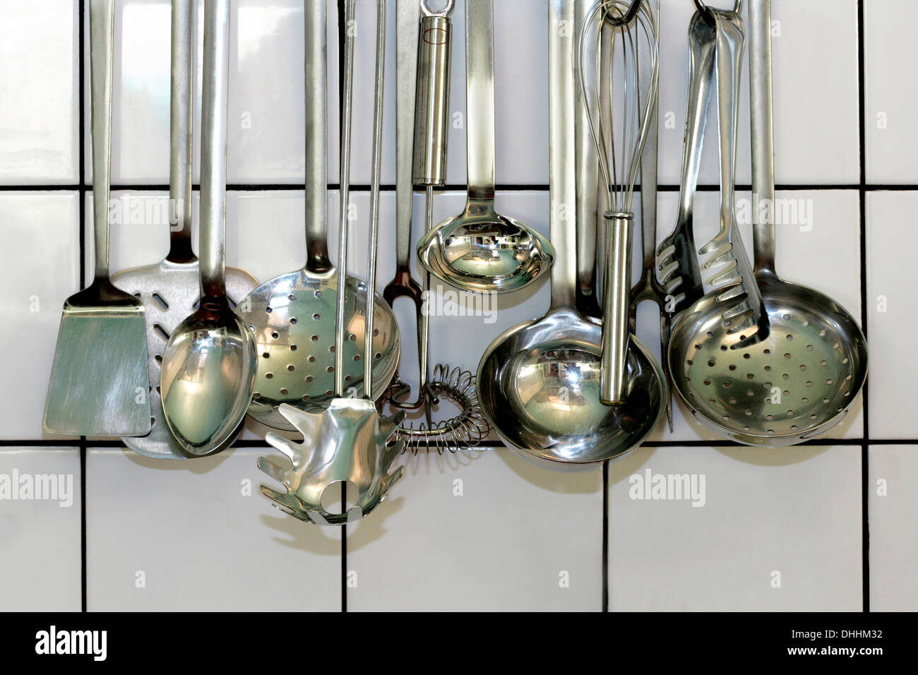 Various kitchen ladles hanging in front of a white tiled wall, Germany