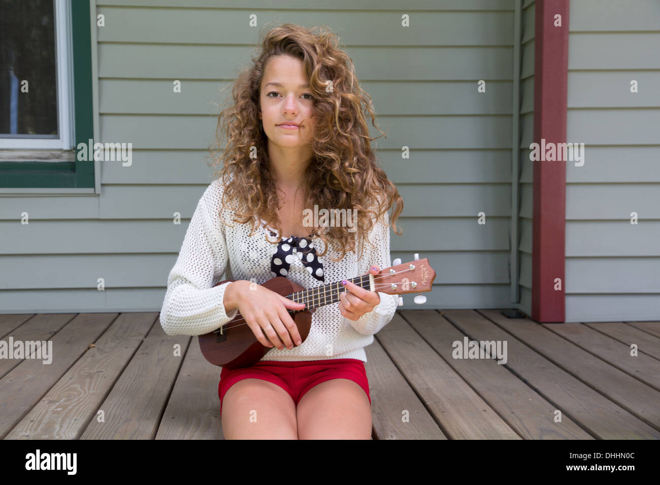 Teenage girl sitting on porch holding miniature guitar Stock Photo