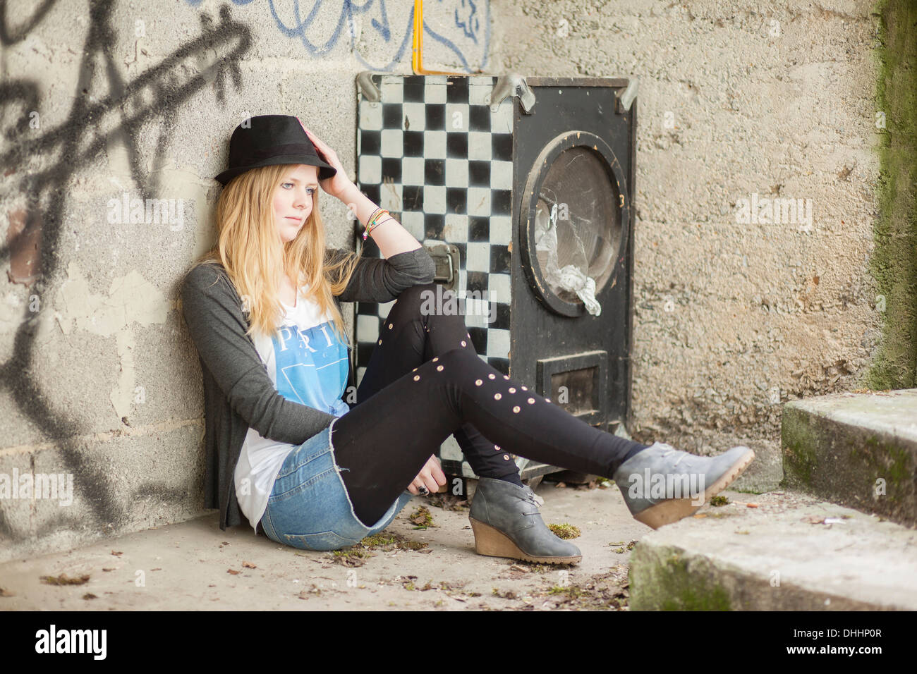 Young woman wearing a hat posing in front of a wall with graffiti, Hesse, Germany Stock Photo