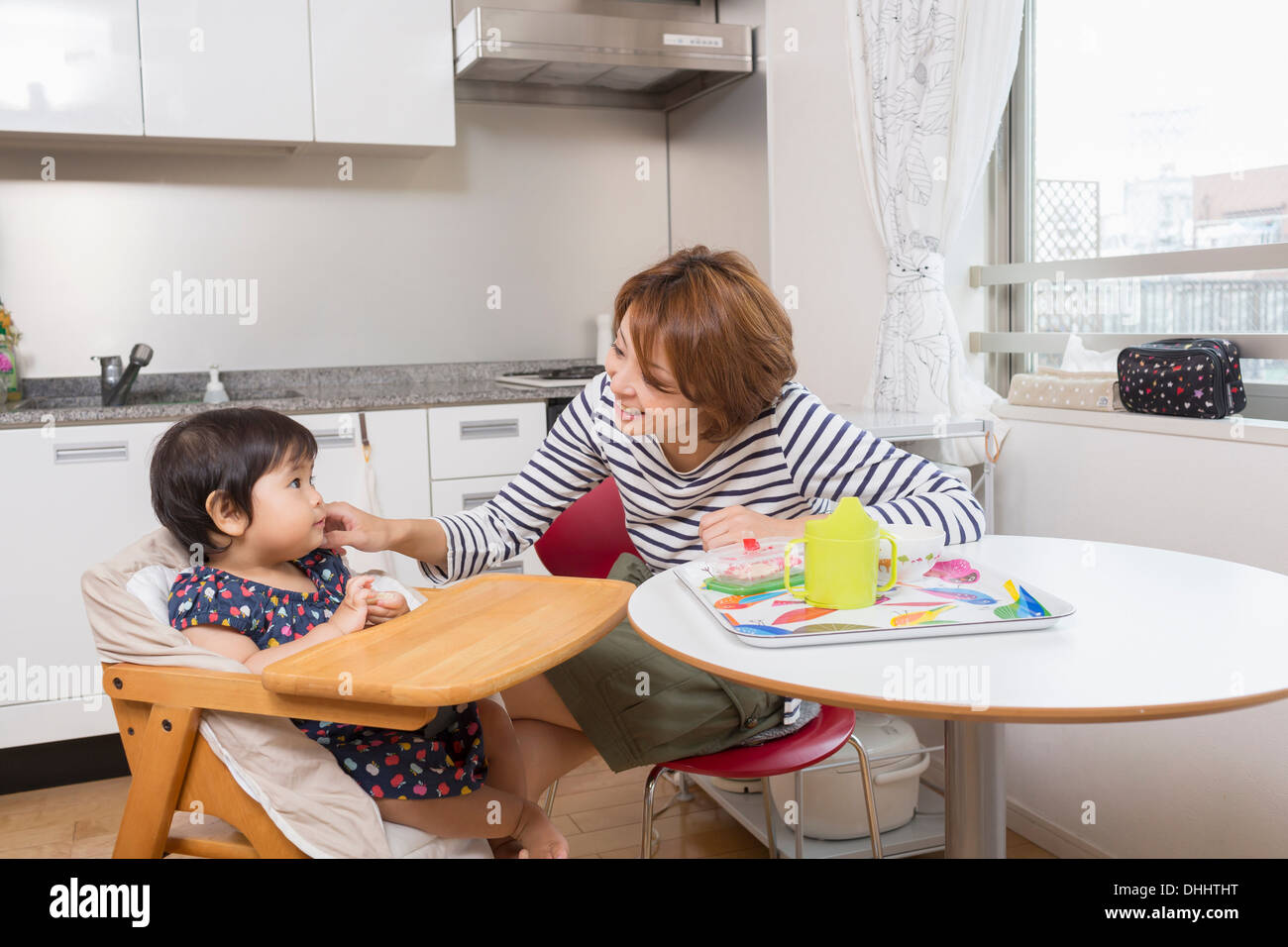 Mother chatting to baby at dining table Stock Photo