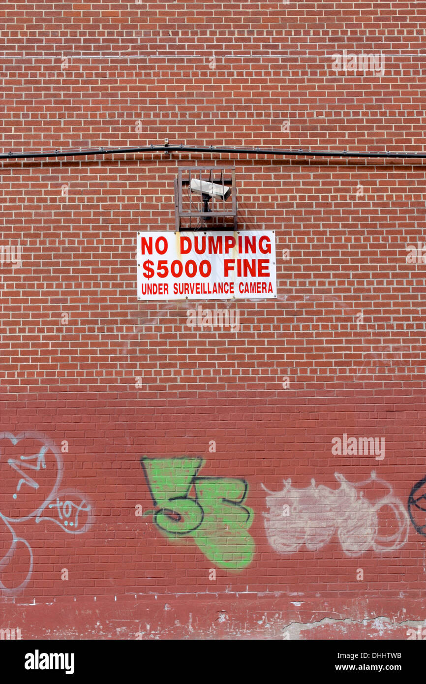 Brick wall with graffiti and a no dumping $5,000 fine sign and surveillance camera in Brooklyn, New York. Stock Photo