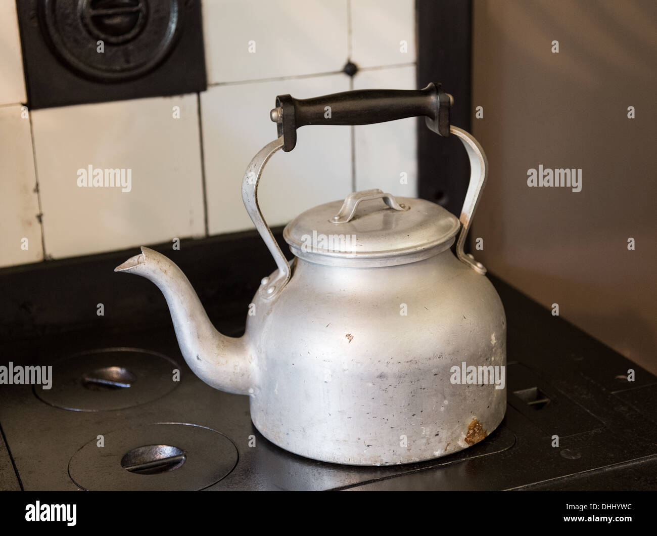 Old-fashioned metal kettle sitting on cast iron cooker hob Stock Photo