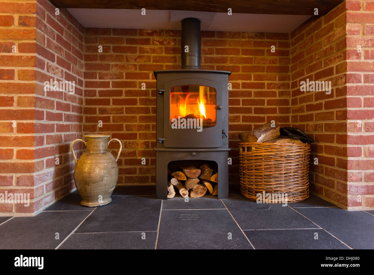 Fire in wood burning stove in brick fireplace with basket of cut wood ready for burning Stock Photo