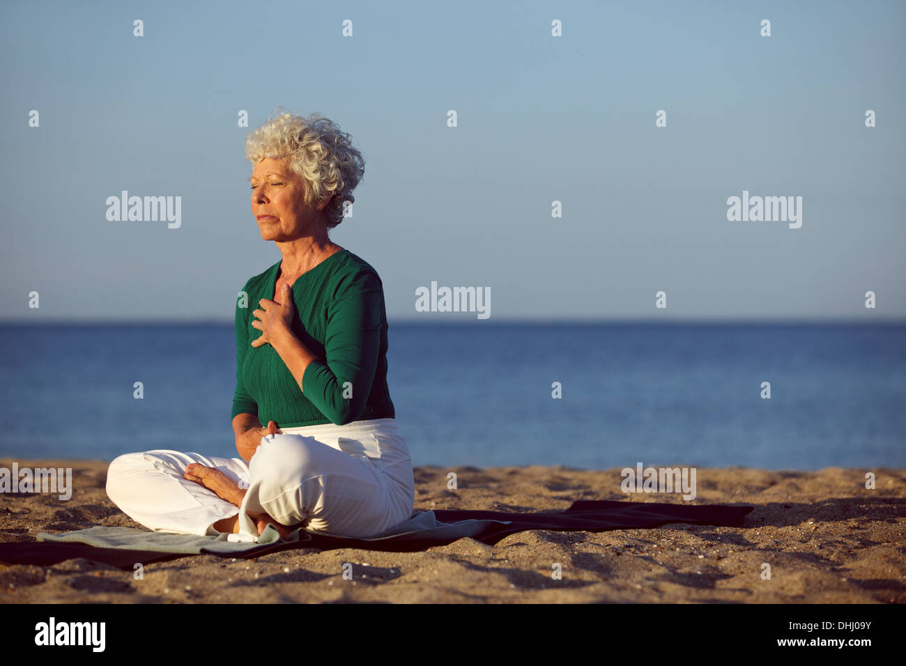 Senior woman in meditation by beautiful ocean. Eldery woman doing yoga on beach. Stock Photo