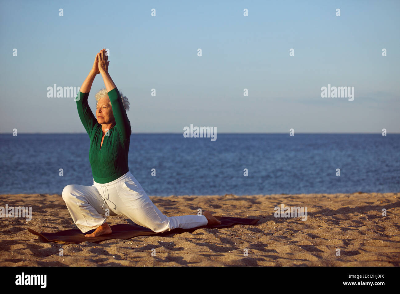 Senior woman practicing yoga on beach. Elderly woman doing yoga exercise on sandy beach. Yoga and relaxation concept. Stock Photo