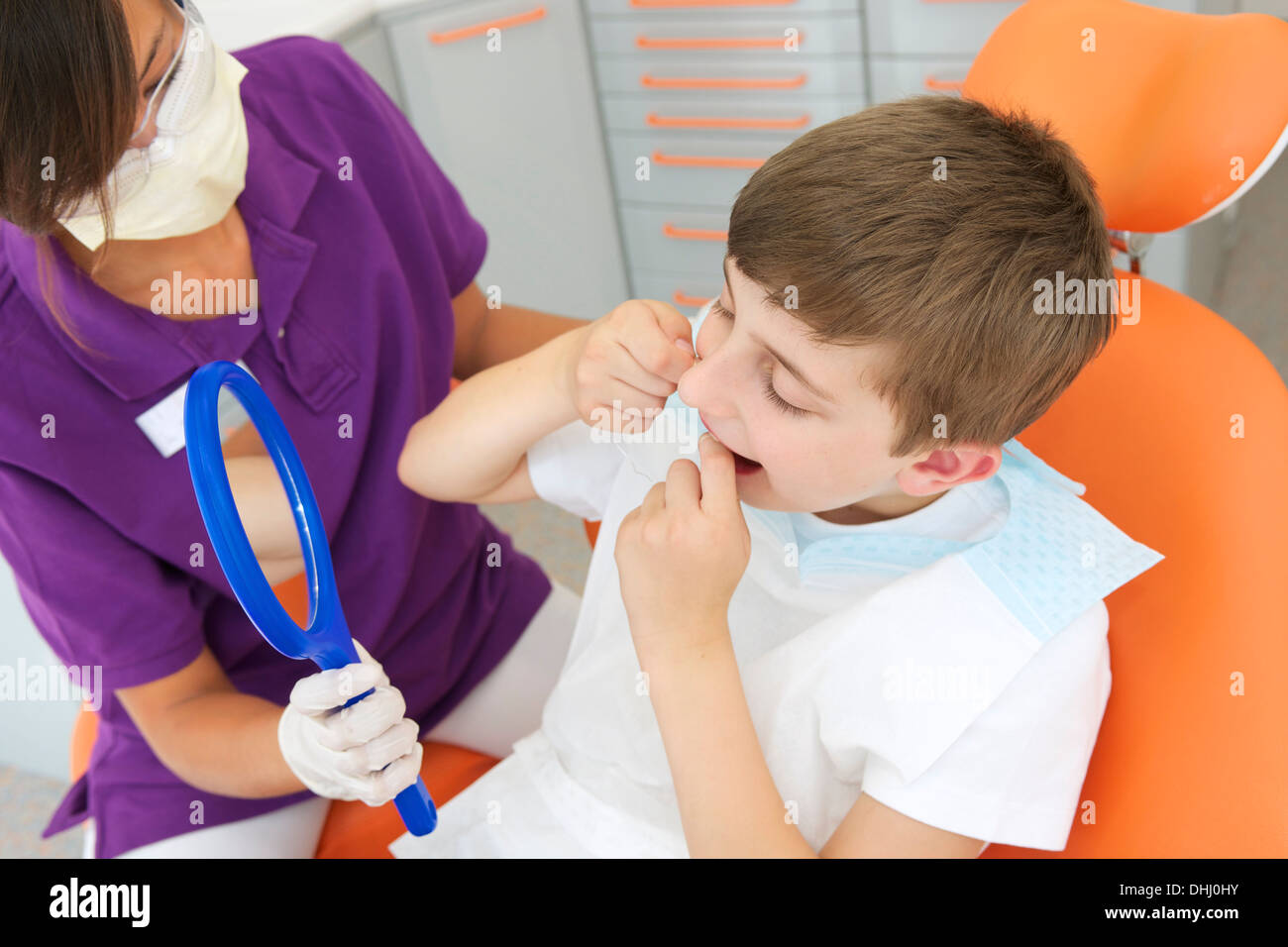 Dental hygienist holding hand mirror while patient flosses Stock Photo