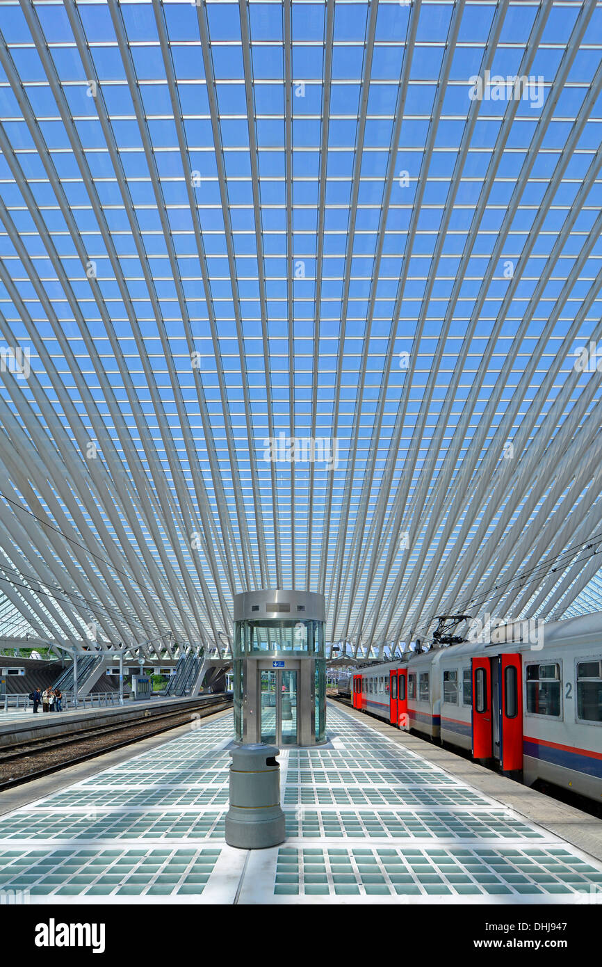 Huge symmetrical glass roof building curves over modern public transport Liège train station platform & railway tracks few people quiet summer Sunday Stock Photo