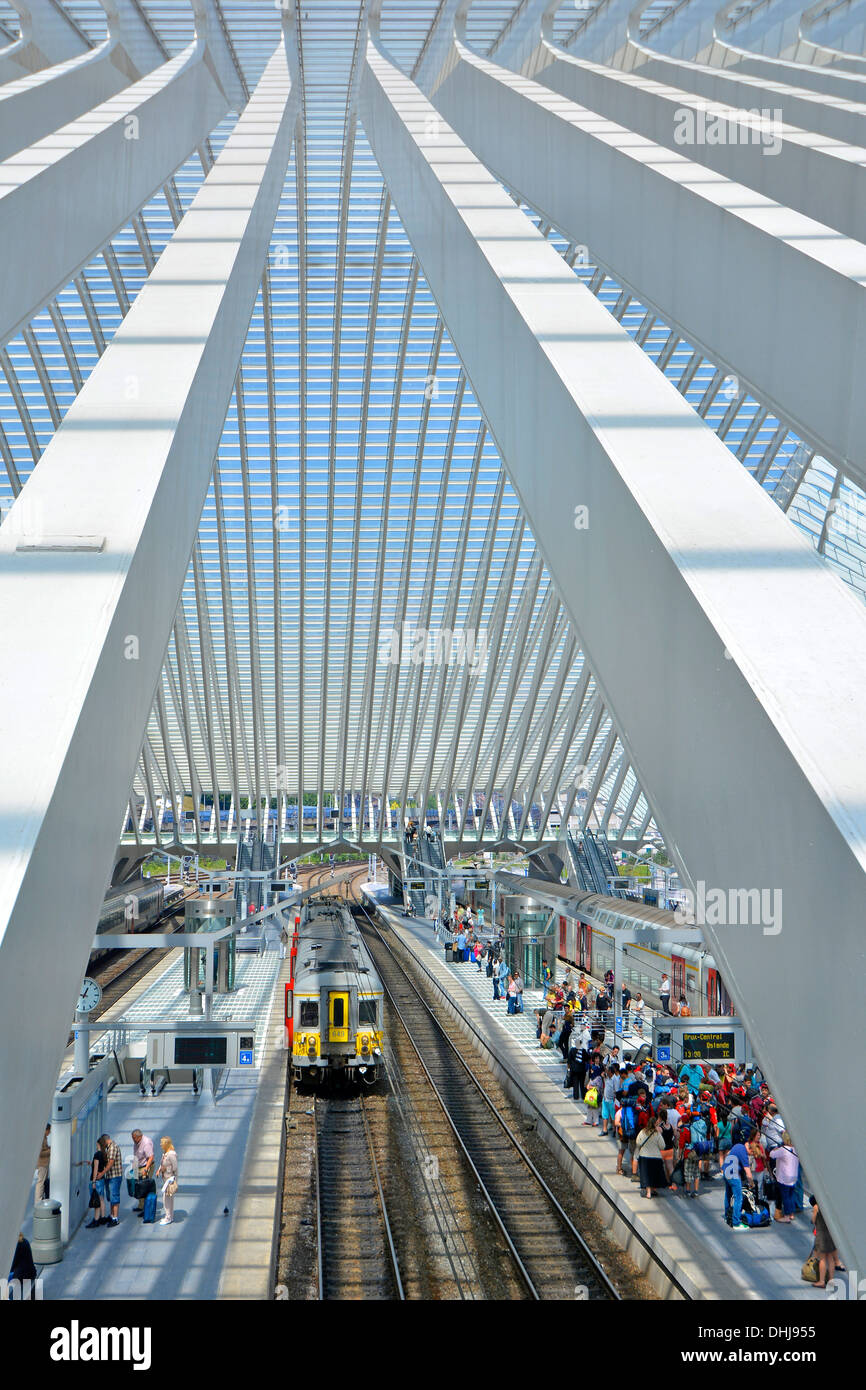 Public transport aerial view from above looking down between beams at Belgium passenger train & Liege station platform people waiting under glass roof Stock Photo