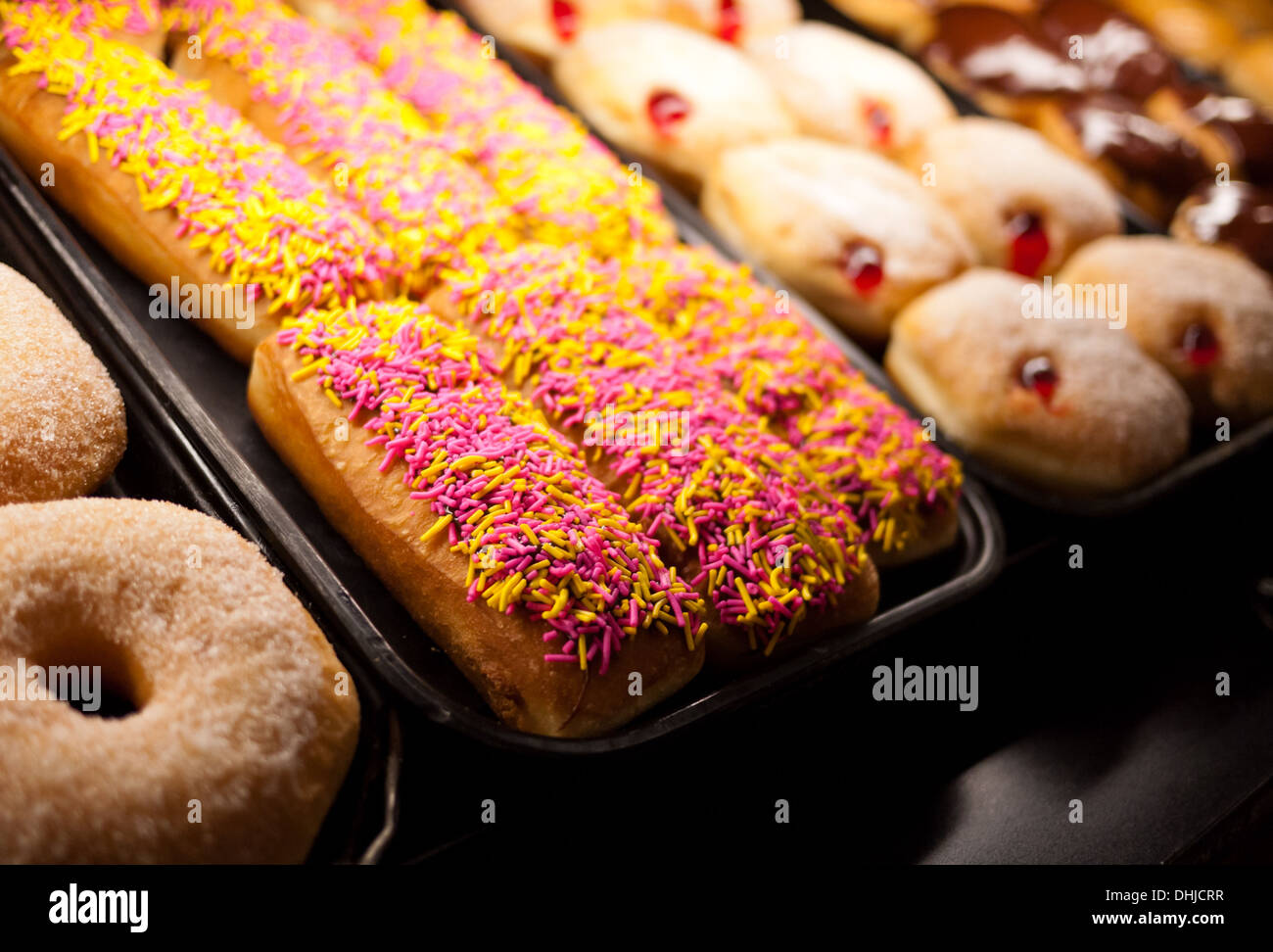 Sprinkle donuts, sugar donuts, and powdered jelly filled donuts in a bakery window. Stock Photo