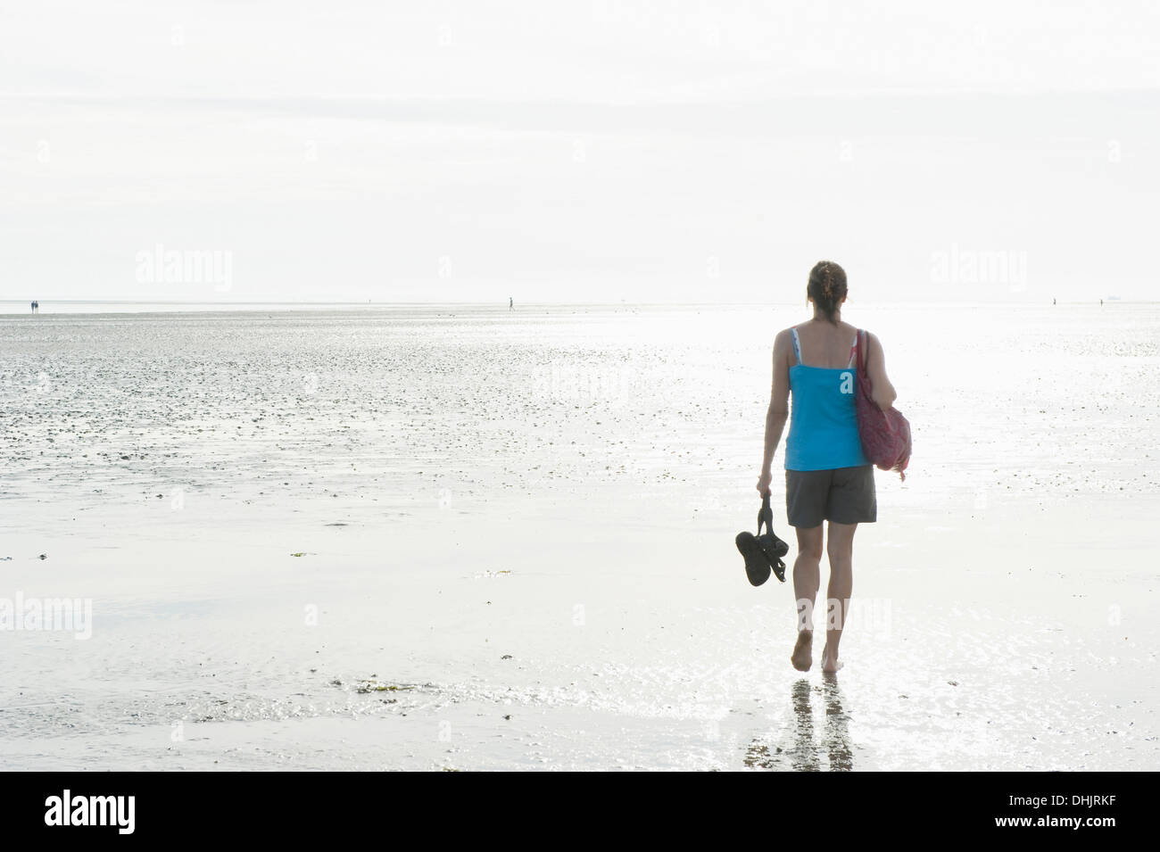 Woman walking barefooted through intertidal mudflats, Wattenmeer National Park, near Wyk, Foehr, North Frisian Islands, Schleswi Stock Photo