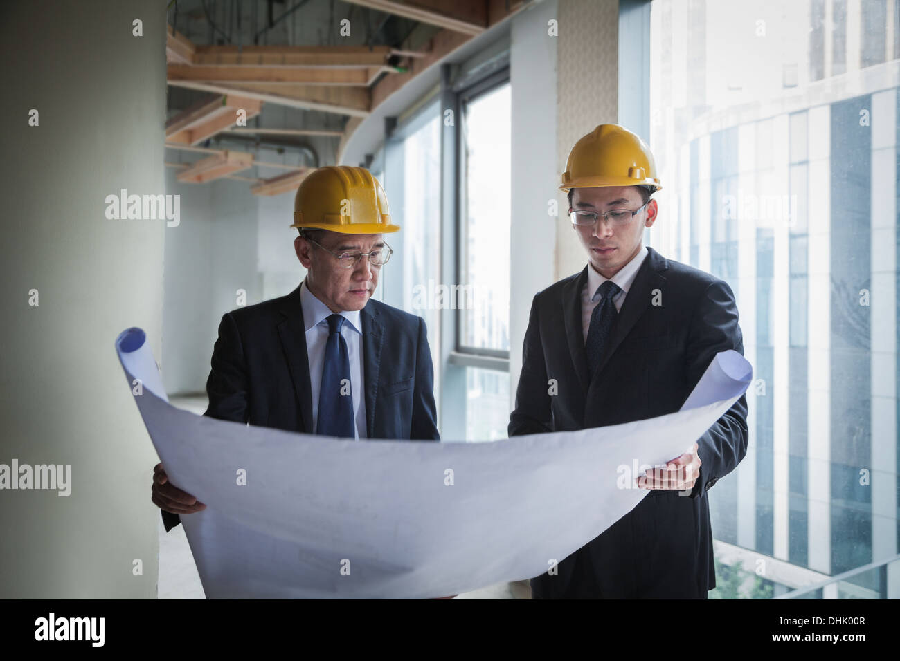 Two architects in hardhats examining a blueprint in an office building Stock Photo