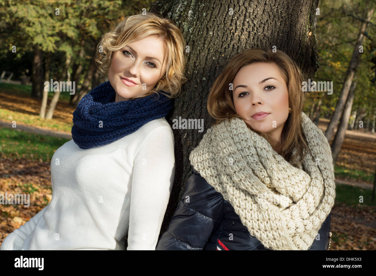 Two beautiful young women posing in front of a tree in autumn park ...