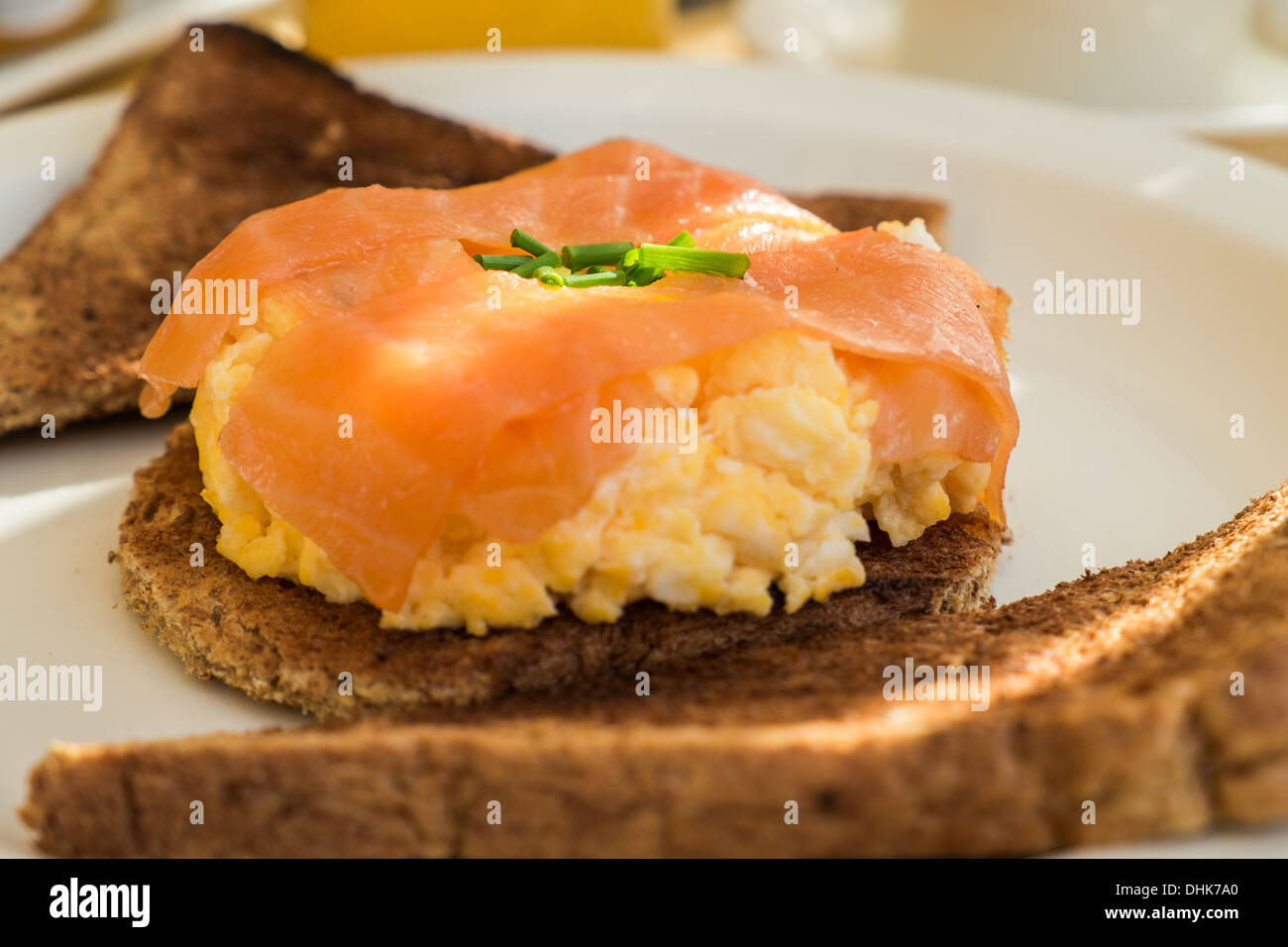 Smoked salmon breakfast on scrambled eggs and toast with a ray of sun across the white plate Stock Photo