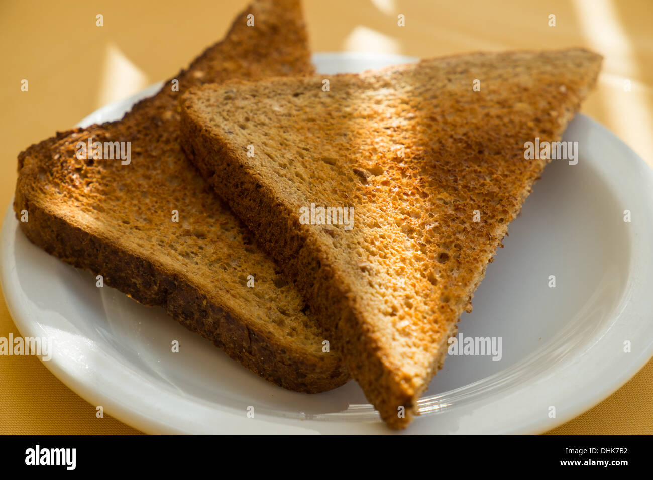 Two slices of brown toast sitting on a white plate with rays of sun across them. Stock Photo