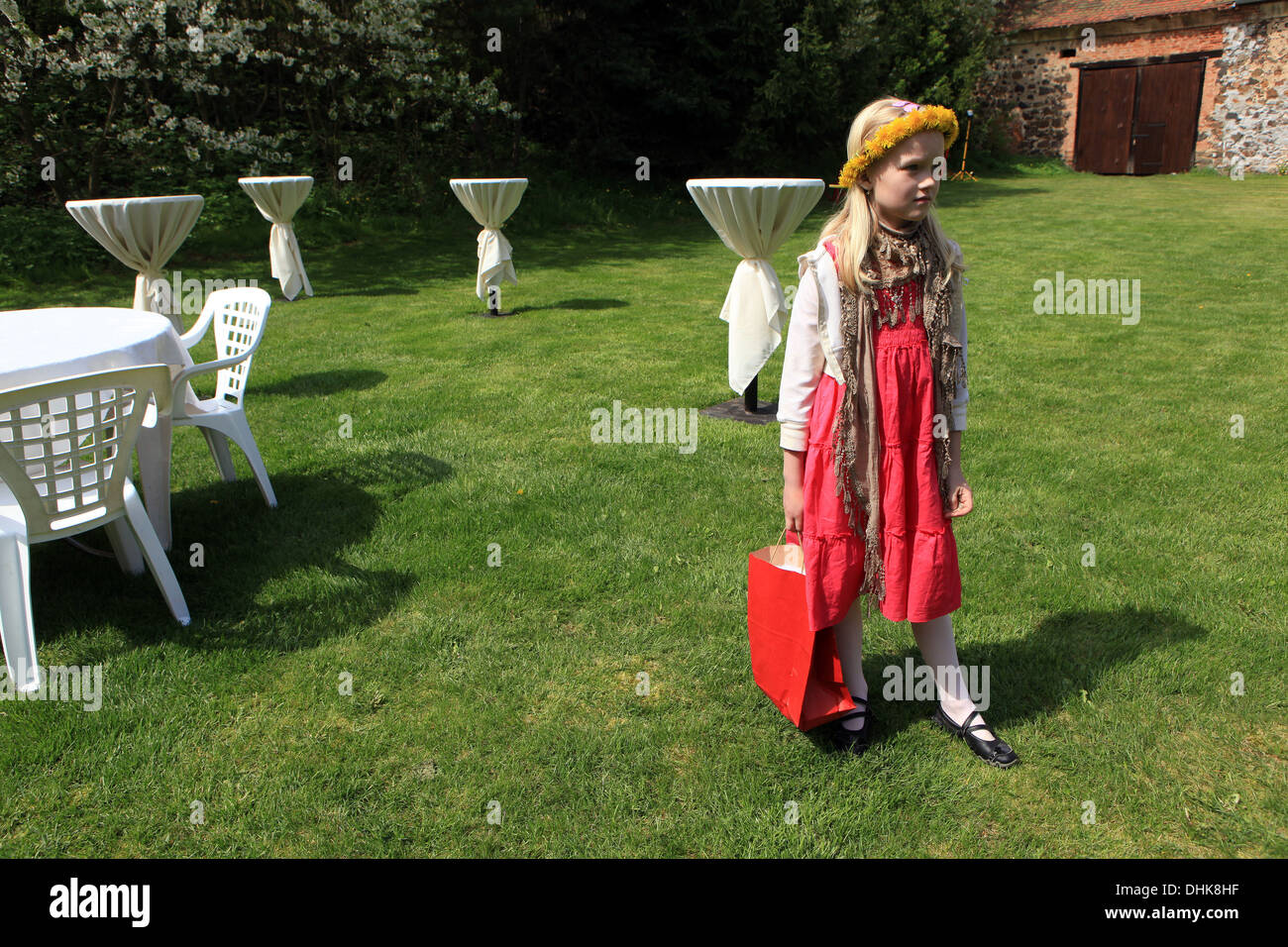 Little girl with dandelion wreath, garden with white tables Stock Photo