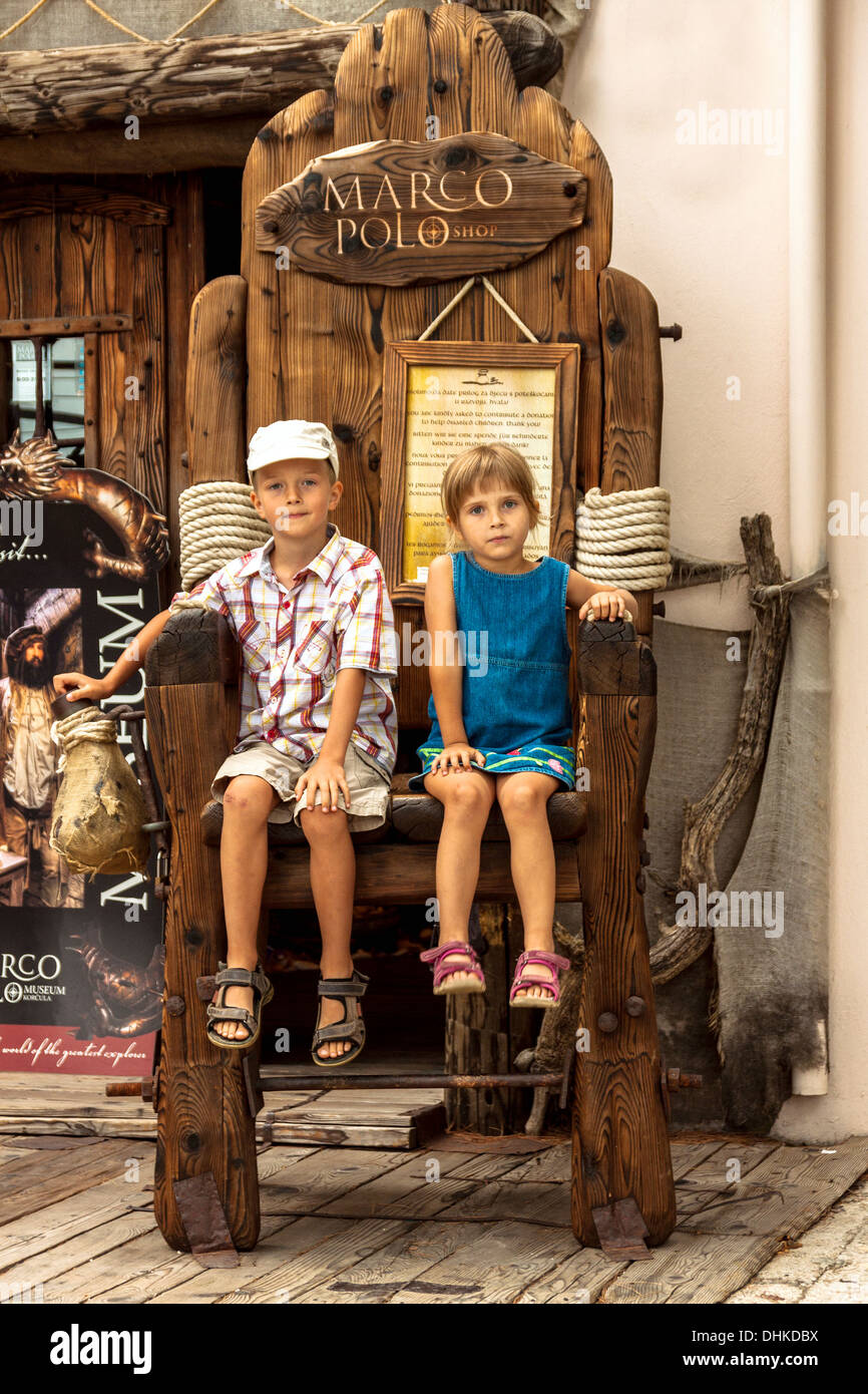 Children sitting on a huge chair in front of Marco Polo shop in Korcula,  Croatia Stock Photo - Alamy