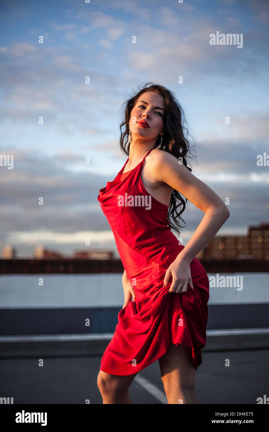 Portrait of a woman standing, hiking up her red dress, London, England, UK. Stock Photo