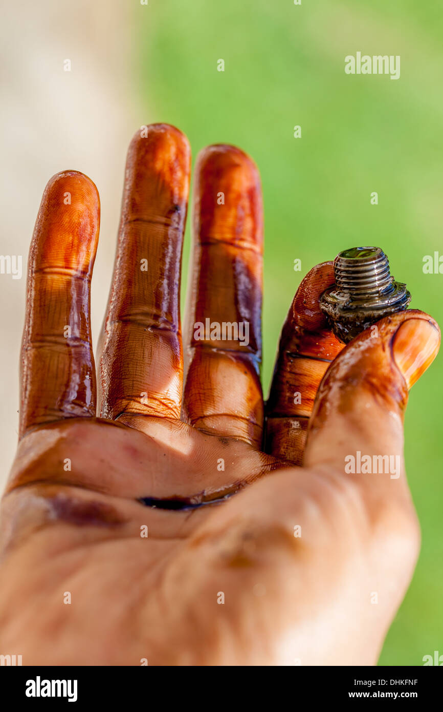 hand holding bolt and covered in car engine oil. Stock Photo