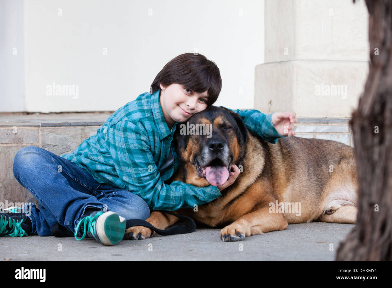A 10 year old boy and his dog sitting down on the sidewalk Stock Photo
