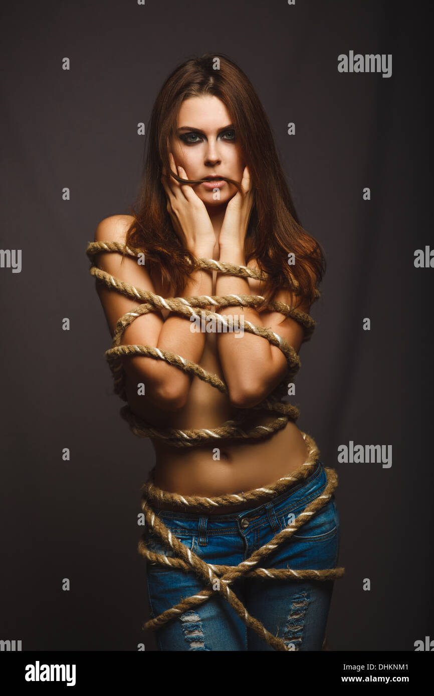 brunette woman bound with rope prisoner in jeans on a gray background Stock  Photo - Alamy