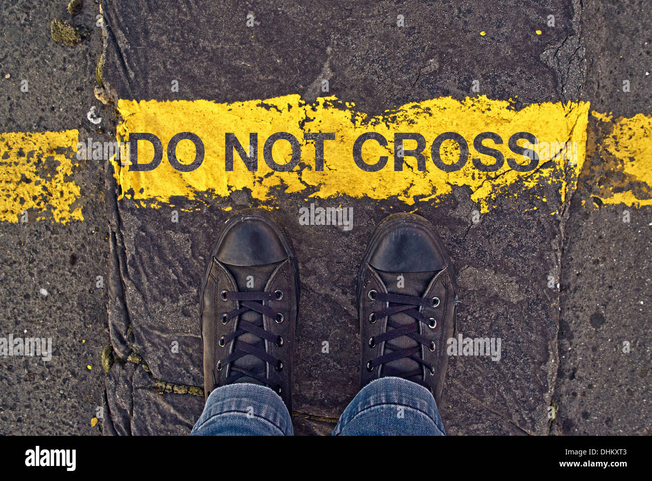 Male sneakers on the asphalt road with yellow line and title Do Not Cross. Border line concept, danger or warning sign. Stock Photo