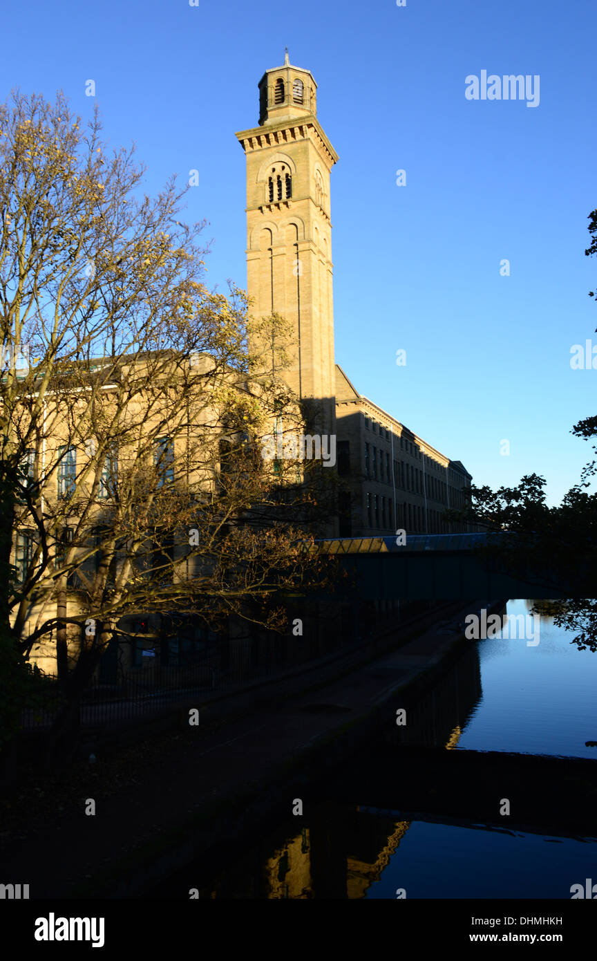A deep blue reflection of the canal which emulates the sky in this shot of a Mill Complex in Saltaire, Shipley Stock Photo