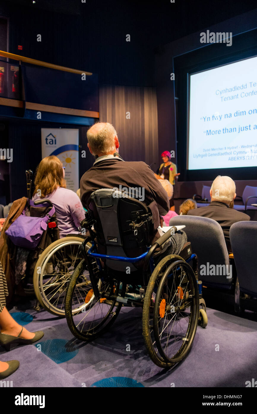 Rear view of two adults in wheelchairs attending  a social housing landlord, tenants conference meeting Stock Photo