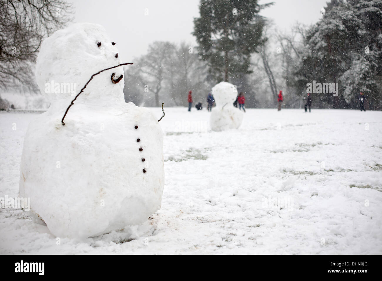 Snowman in parkland setting with people having a snowball fight in the distance Stock Photo