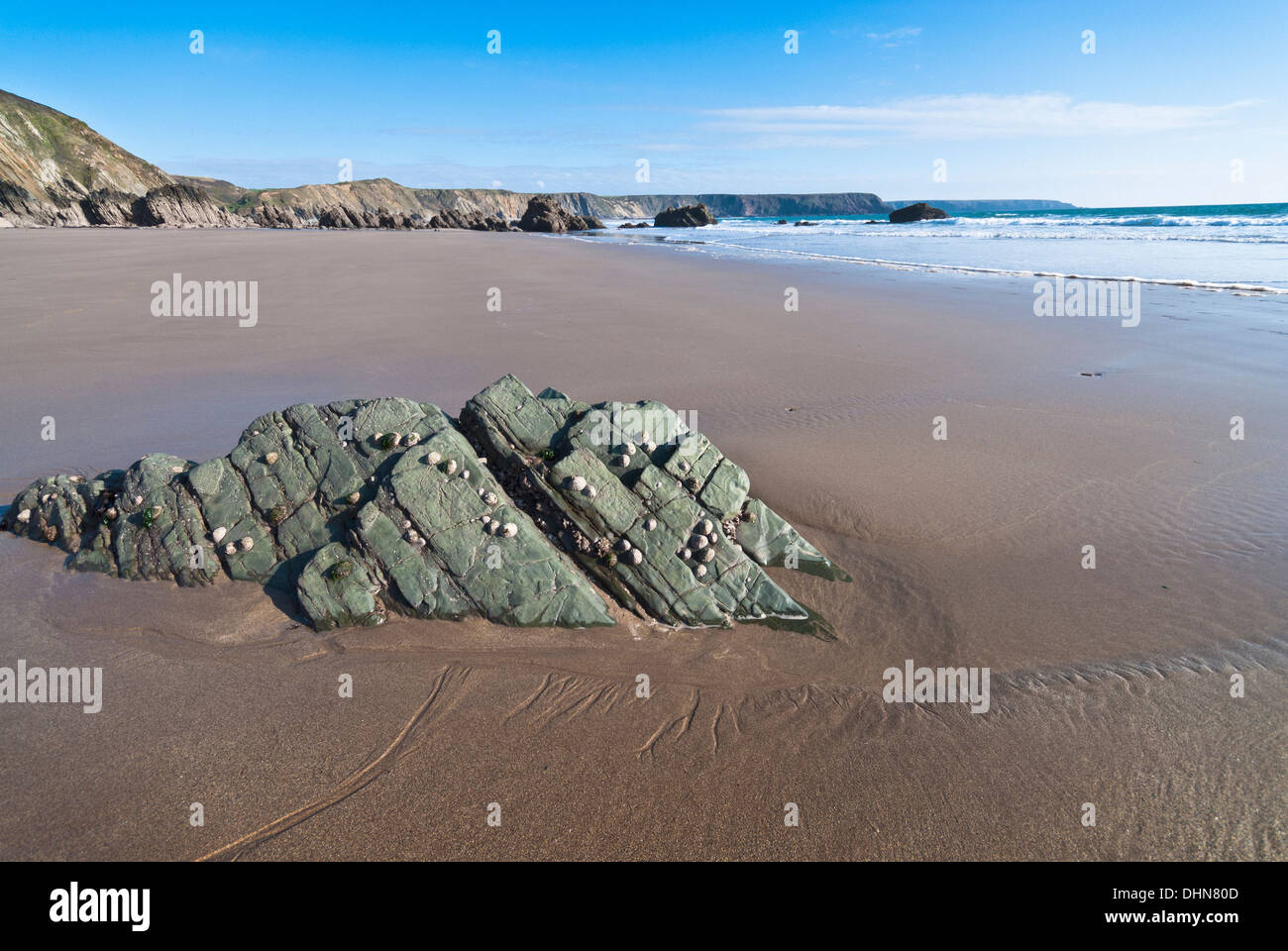 Deserted pristine beach at Marloes in Pembrokeshire at low tide with a rock outcrop in the foreground on a sunny day. Stock Photo