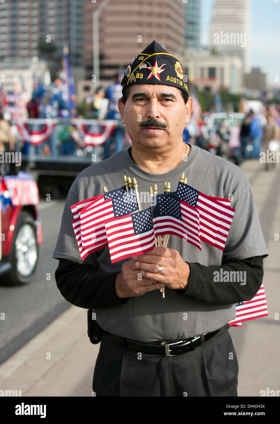 Male Hispanic military veteran holds several small American flags during a Veteran's Day parade in Austin, Texas Stock Photo