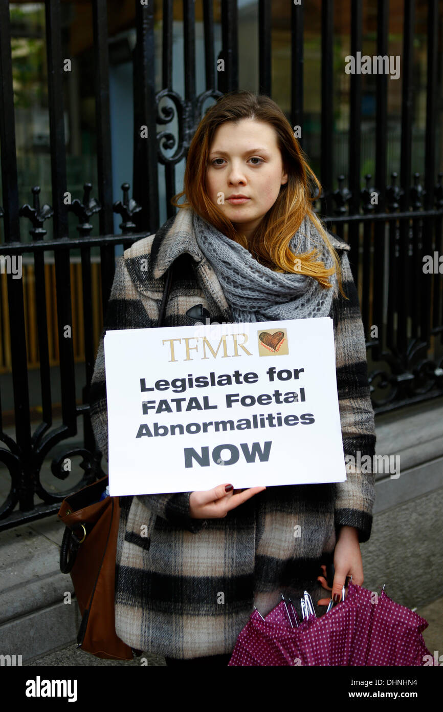 Dublin, Ireland. 13th November 2013. A protester stands outside the Dail (Irish parliament) holding a sign that reads 'TFMR Legislate for FATAL Foetal Abnormalities NOW'. The Center of Reproductive Rights brought a case against Ireland to the UN Human Rights Committee on behalf of Amanda Mellet. She had to travel to the UK for an abortion after she had been diagnosed with fatal fetal abnormality during her pregnancy. Abortions for fatal fetal abnormalities are illegal in Ireland. Credit:  Michael Debets/Alamy Live News Stock Photo