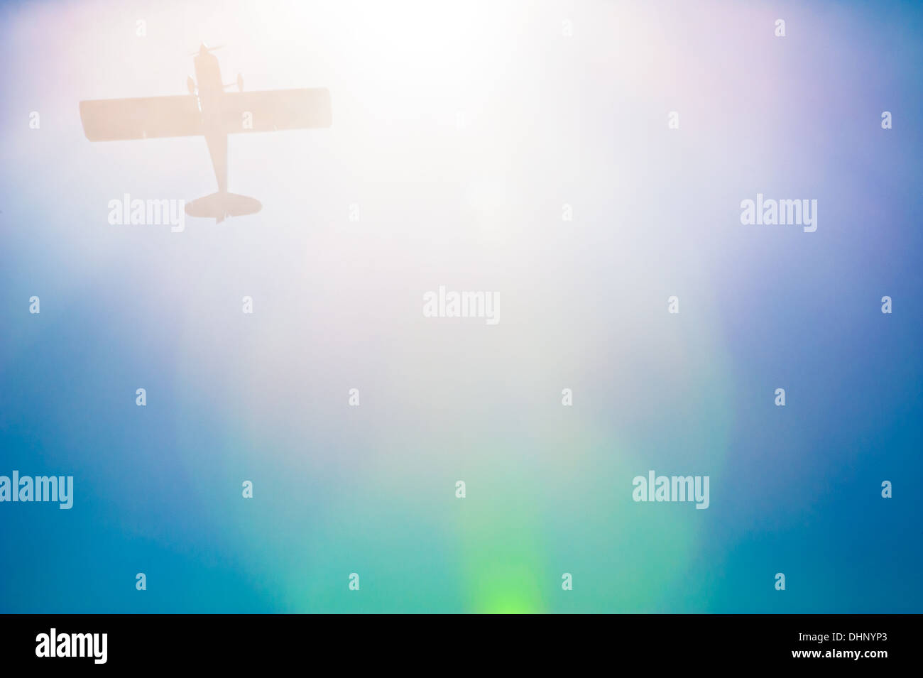 Single prop airplane ghosted by a colorful sun flare in a clear blue sky. (USA) Stock Photo
