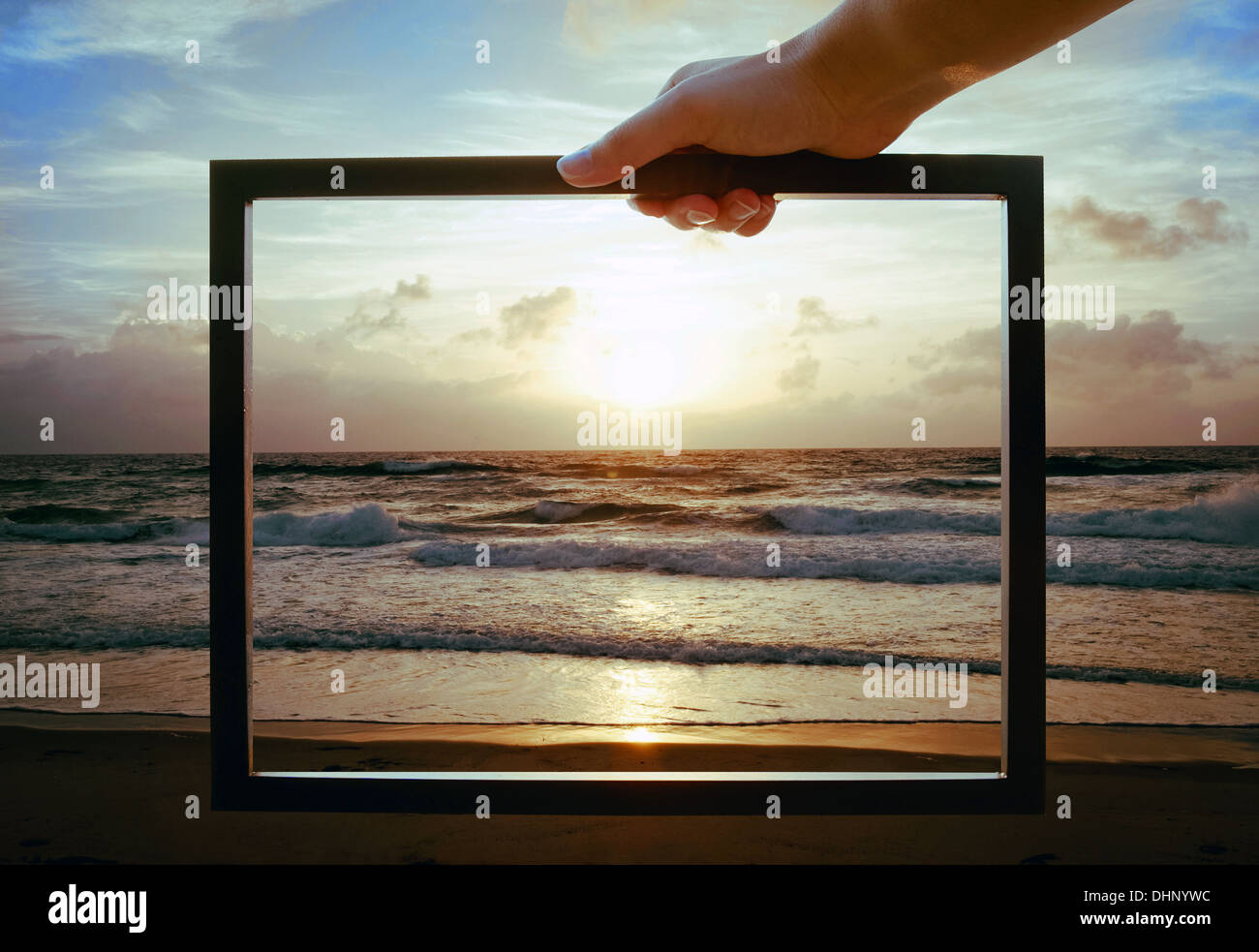 Hand holding a picture frame over the ocean at dusk Stock Photo