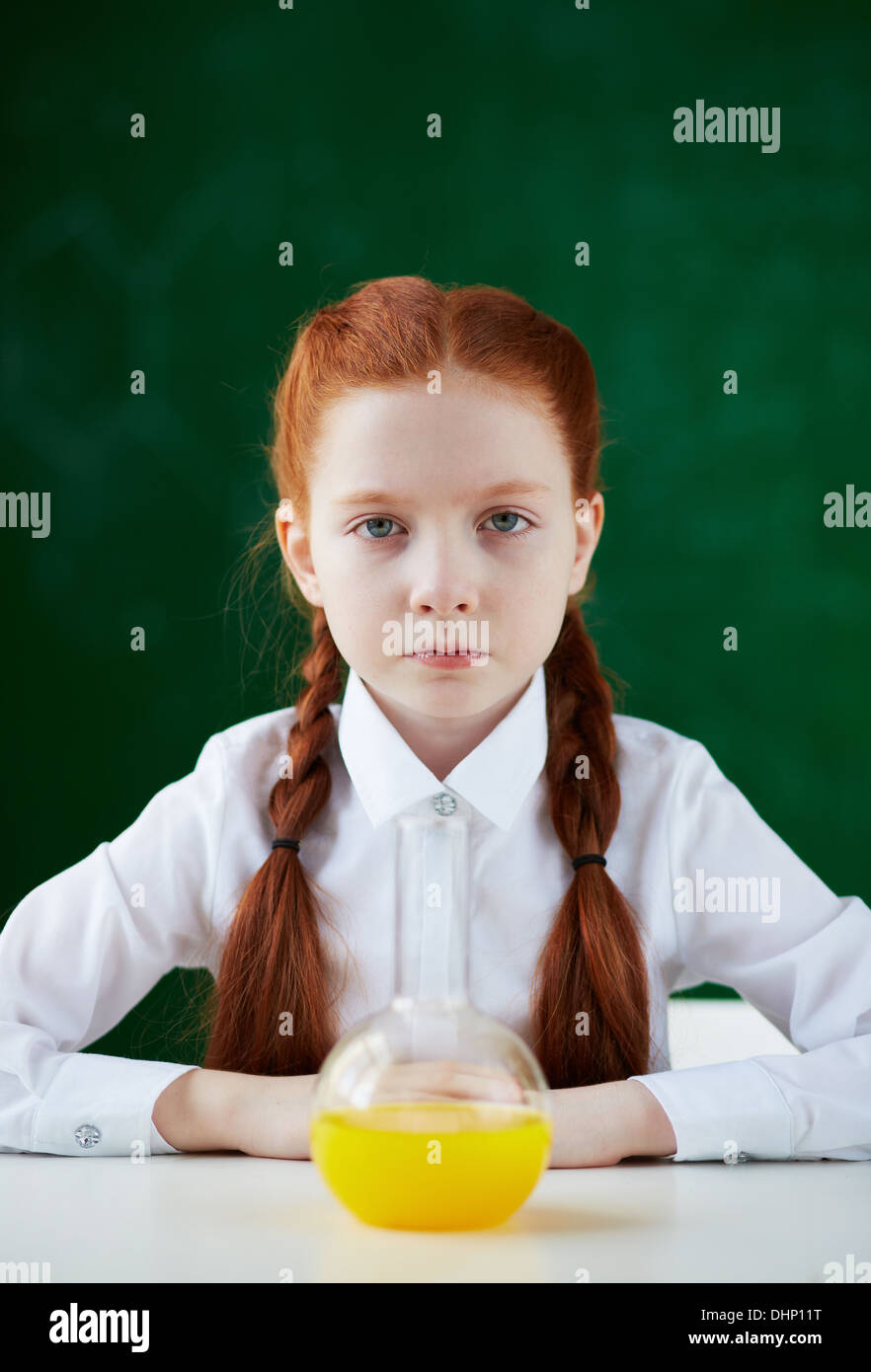 Portrait of schoolgirl sitting at workplace with chemical liquid in front Stock Photo