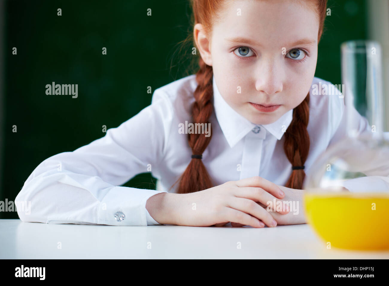 Portrait of schoolgirl sitting at workplace and looking at camera with chemical liquid in front Stock Photo