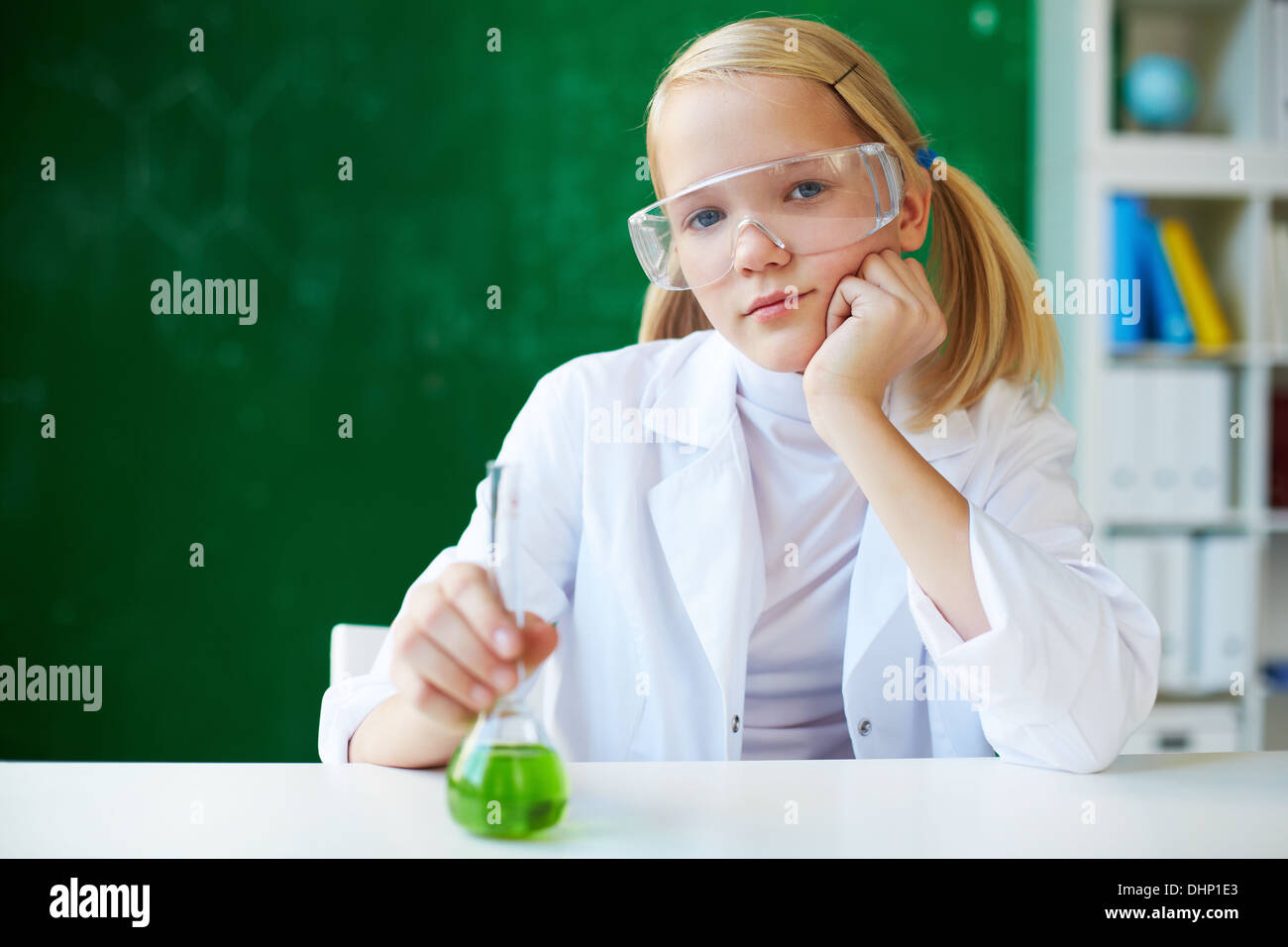 Portrait of cute schoolgirl sitting at workplace with chemical liquid in front Stock Photo