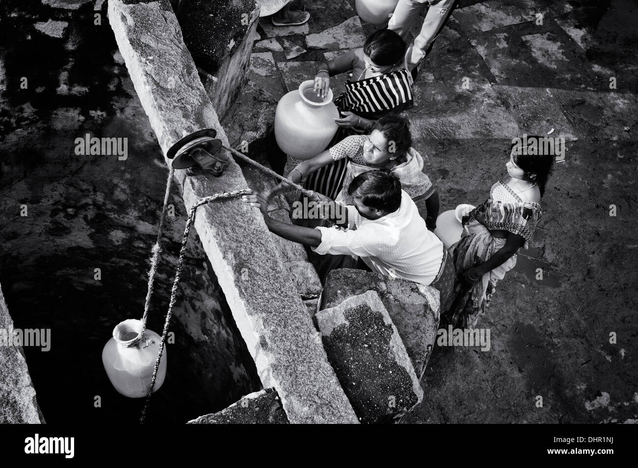 Indian women and men drawing water from a well in a rural Indian village street. Andhra Pradesh, India . Monochrome Stock Photo