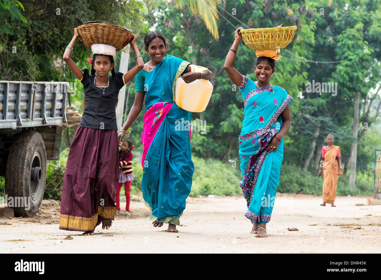 Happy smiling Indian women and girl carrying a water jug and baskets in a rural Indian village street. Andhra Pradesh, India Stock Photo