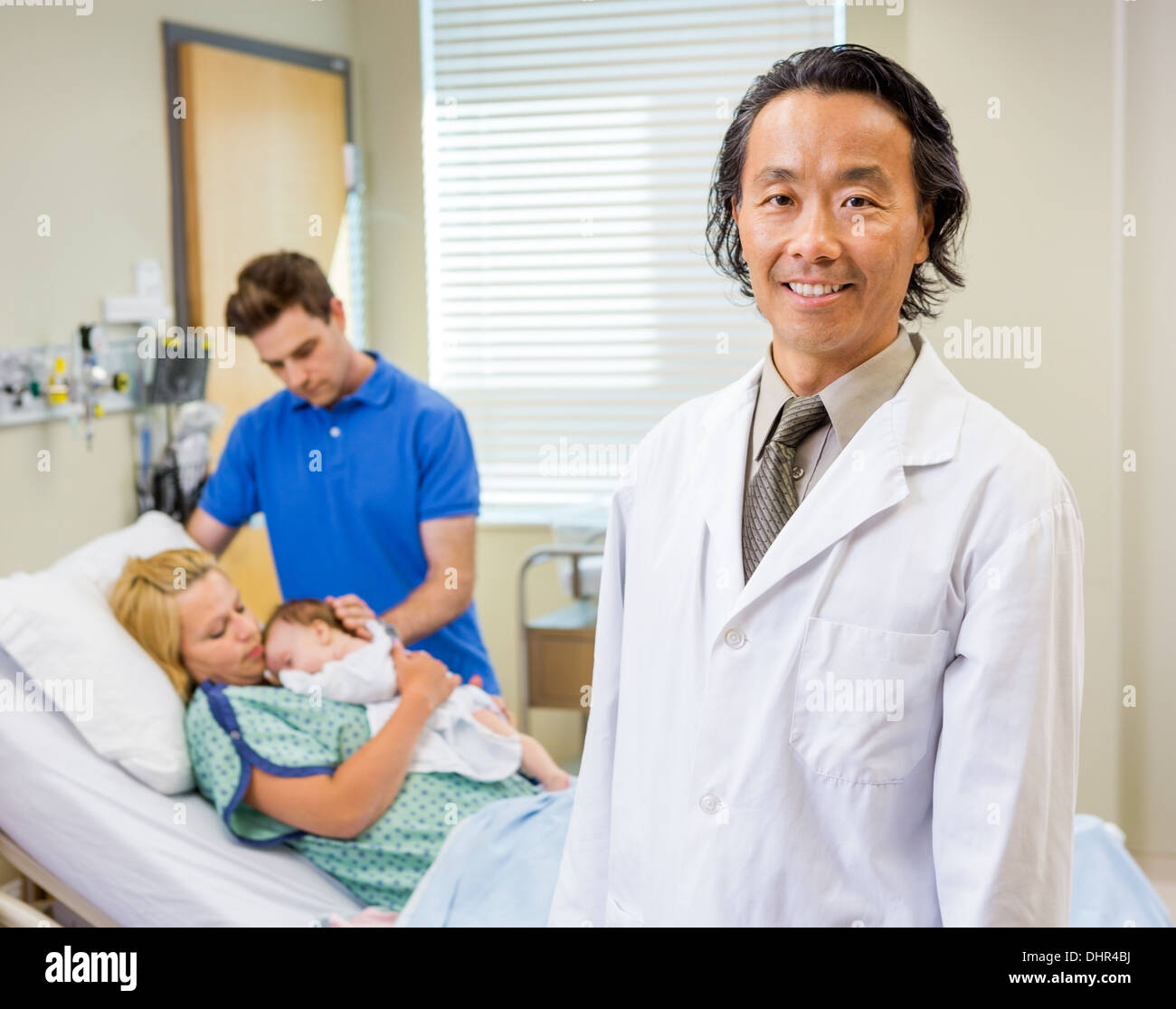 Mature Doctor Standing With Couple And Newborn Baby In Backgroun Stock Photo