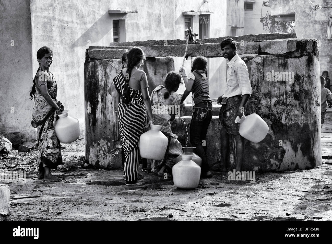 Indian women, men and children drawing water from a well in a rural Indian village street. Andhra Pradesh, India . Monochrome Stock Photo